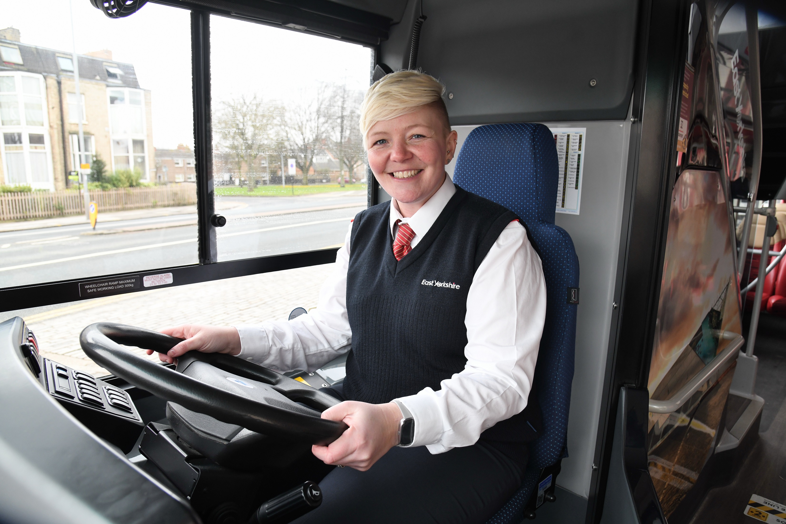 Woman with blonde short hair sat in bus driver cab
