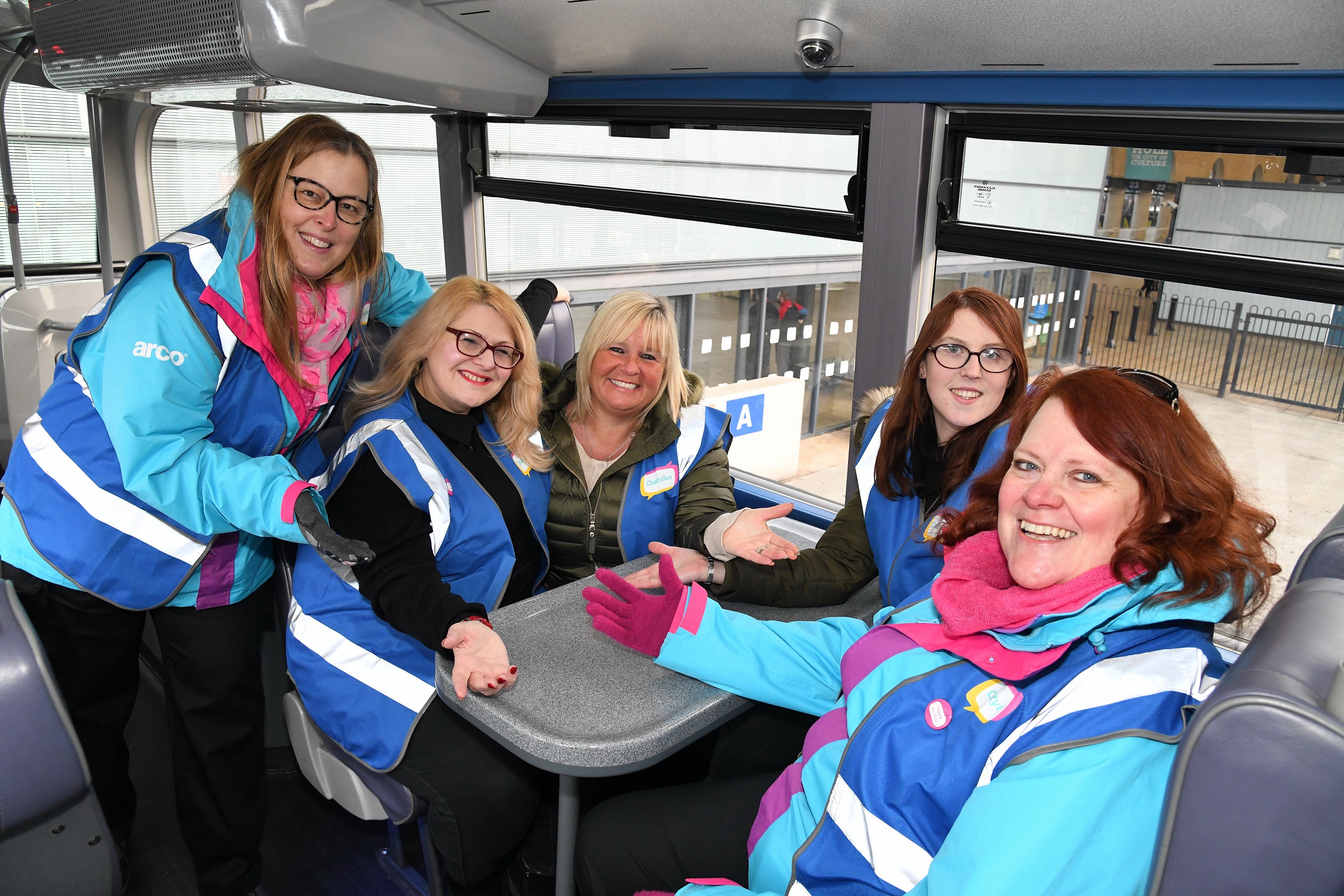 Five people in Chatty Bus clothing sit on a bus, smiling